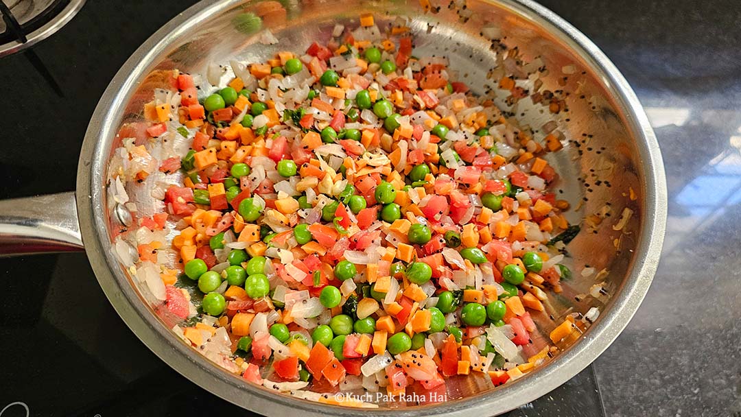 Cooking carrot peas tomatoes in pan.