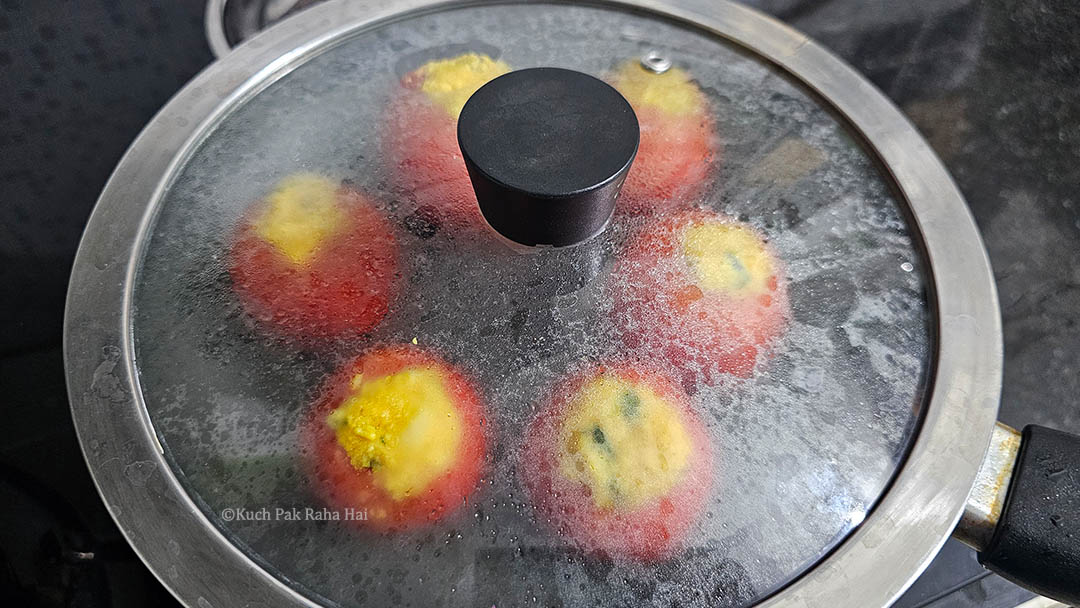 Cooking stuffed tomatoes in a pan on stovetop.