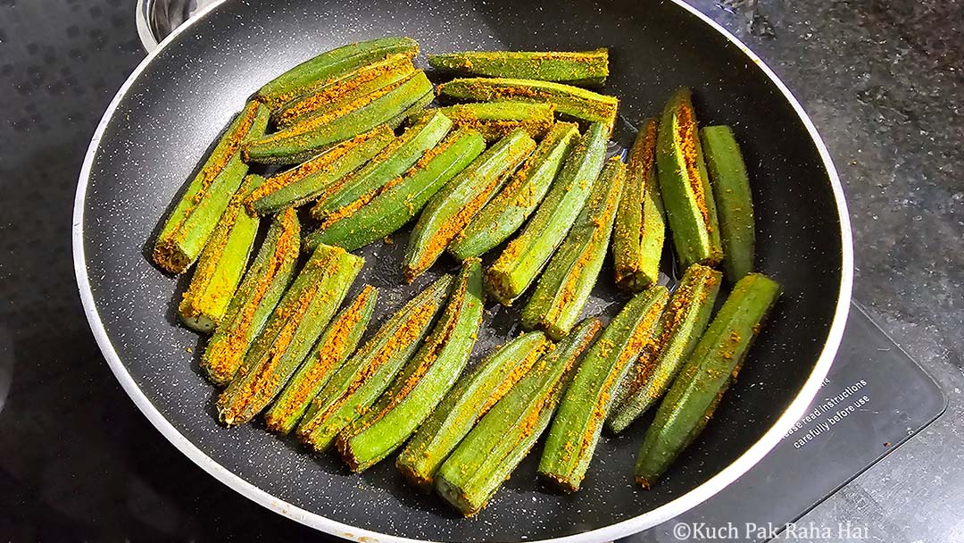 Cooking bharwa bhindi in a pan.