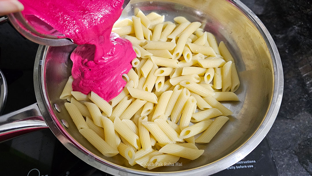 Pouring beetroot sauce over cooked pasta.