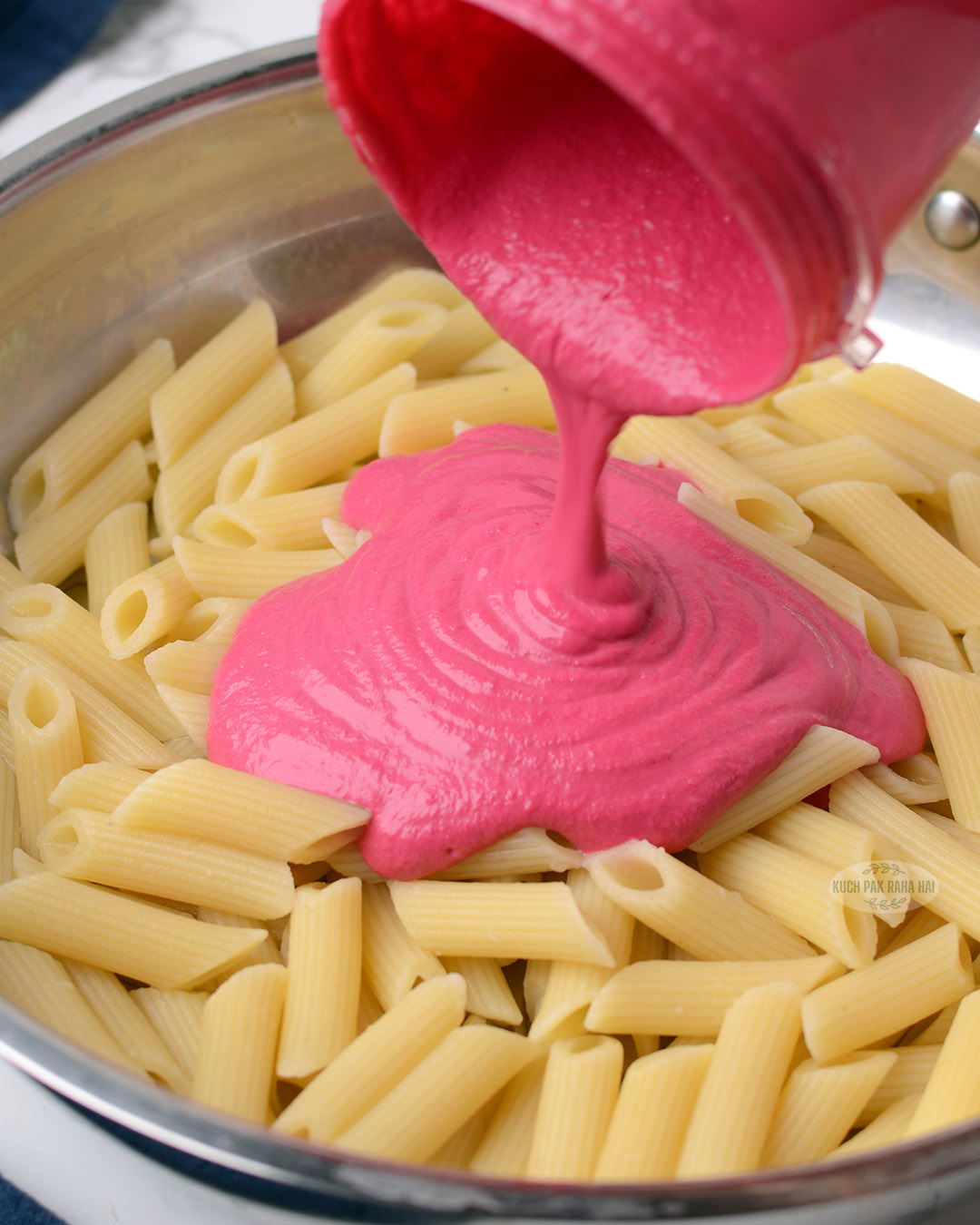 Pouring blended beetroot sauce over pasta.