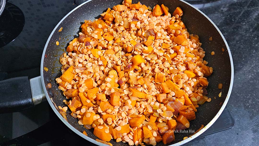 Adding red lentils to sautéed carrots ginger.