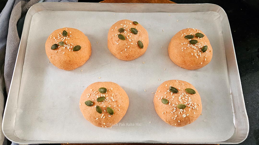 Placing bread rolls on baking tray and sprinkling seeds on them.